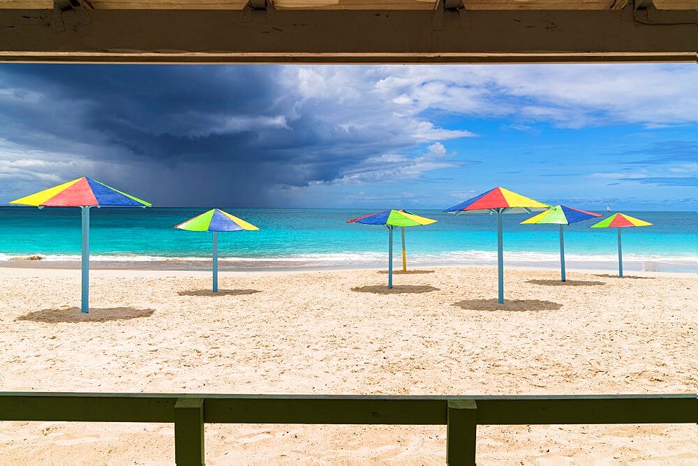 Multicolored striped umbrellas on white sand beach under storm clouds, Antigua, Caribbean, West Indies