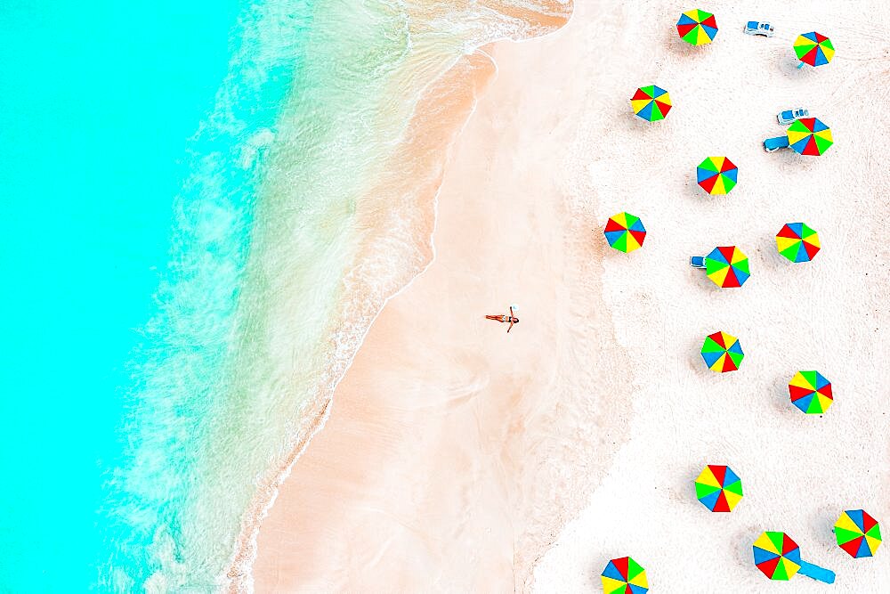 Aerial view of woman with bikini sunbathing on a tropical beach next to colorful umbrellas, Antigua, Caribbean, West Indies