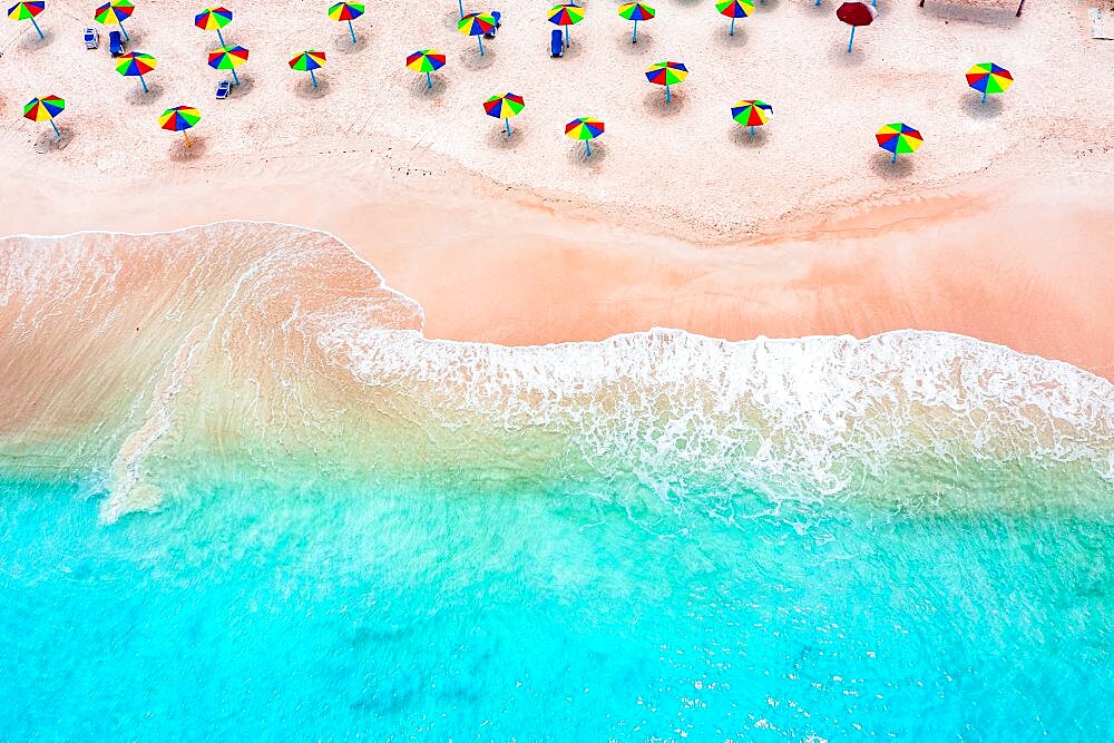 Multi colored umbrellas on tropical beach washed by waves of Caribbean Sea, aerial view, Antigua, West Indies