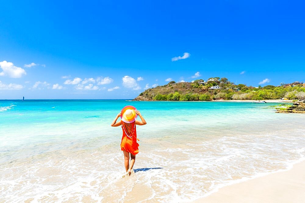 Beautiful woman with orange dress and straw hat standing on a tropical beach, Antigua, Caribbean, West Indies