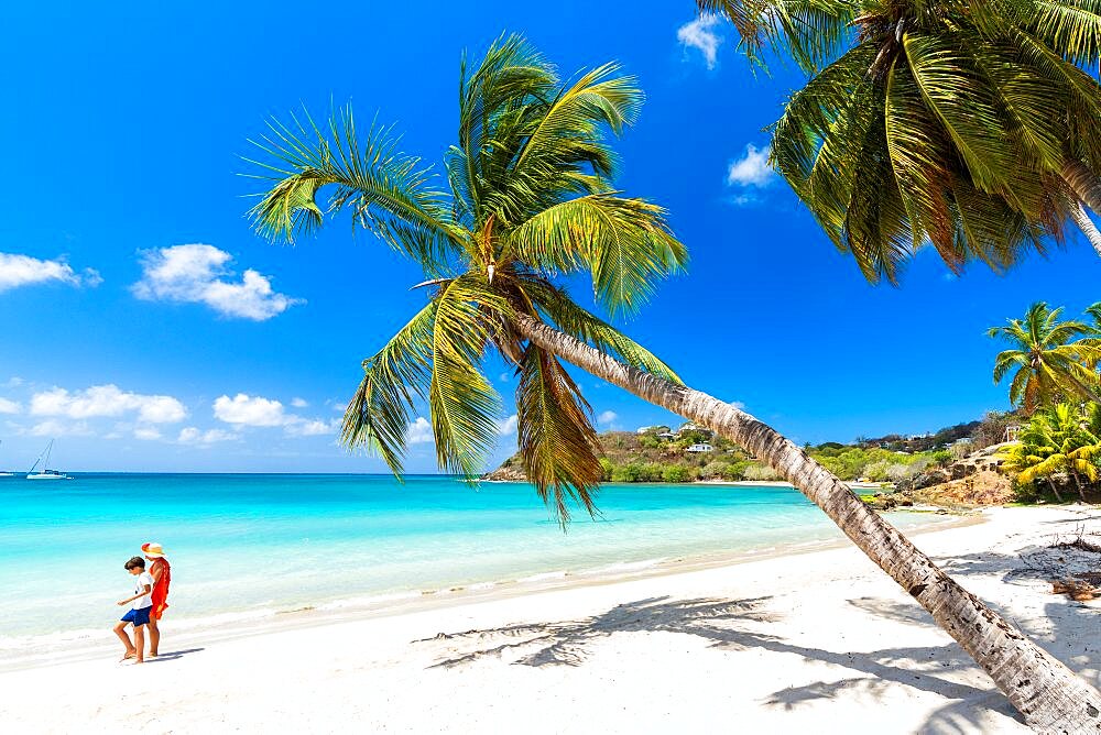 Cheerful little boy with mother walking on idyllic palm fringed beach, Antigua, Leeward Islands, Caribbean, West Indies