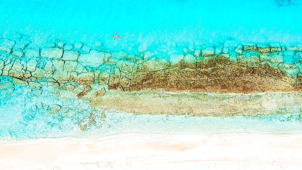 Aerial view of woman floating on the crystal sea in between coral reef and white sand beach, Antigua, Caribbean, West Indies