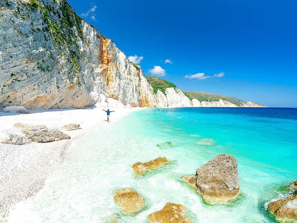 Aerial view of cheerful man with arms outstretched admiring the crystal sea at Fteri Beach, Kefalonia, Ionian Islands, Greek Islands, Greece, Europe