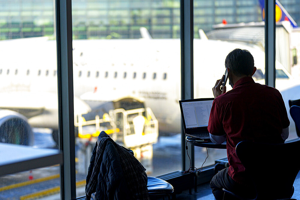 Businessman talking on mobile phone while working on laptop at the airport, Norway, Scandinavia, Europe