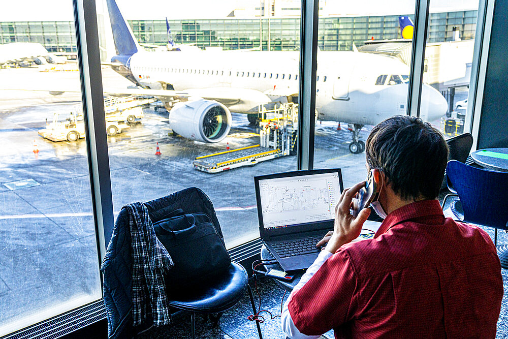 Rear view of mature man using laptop and smartphone while waiting at the airport, Norway, Scandinavia, Europe