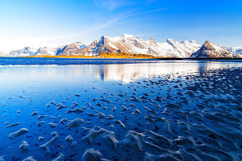 Waves of the cold sea crashing on the beach with snowy mountains on background, Fredvang, Nordland, Lofoten Islands, Norway, Europe