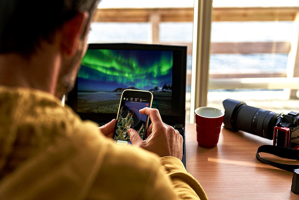 One man looking at maps on smart phone while working with laptop computer, Lofoten Islands, Norway, Scandinavia, Europe