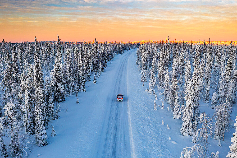 Dramatic sky at dawn over a car traveling into the snowy forest, aerial view, Kangos, Norrbotten County, Lapland, Sweden, Scandinavia, Europe