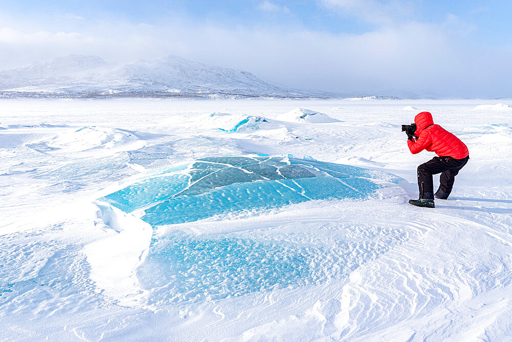 Man photographing the Arctic landscape covered with snow standing on a frozen lake, Norrbotten County, Lapland, Sweden, Scandinavia, Europe