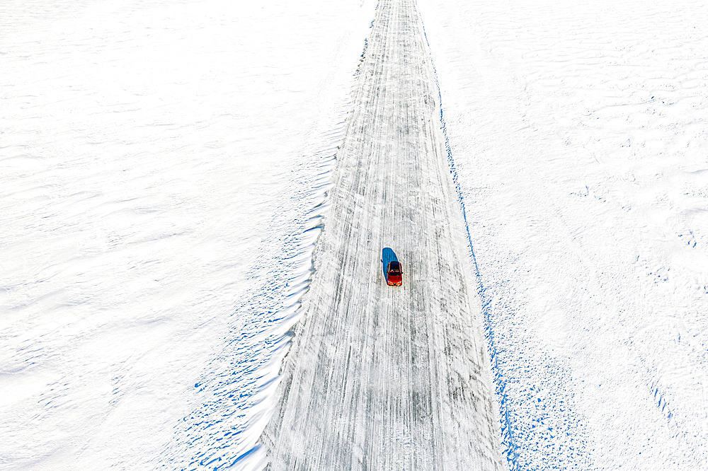 Cold winter sun over an isolated car traveling on ice road on frozen sea, aerial view, Lulea, Norrbotten County, Lapland, Sweden, Scandinavia, Europe