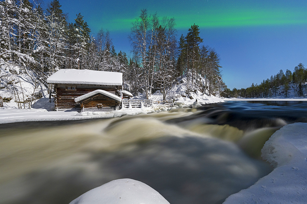 Lone hut in the snowy forest overlooking Myllikoski rapids of frozen river under Northern Lights, Ruka Kuusamo, Lapland, Finland, Europe