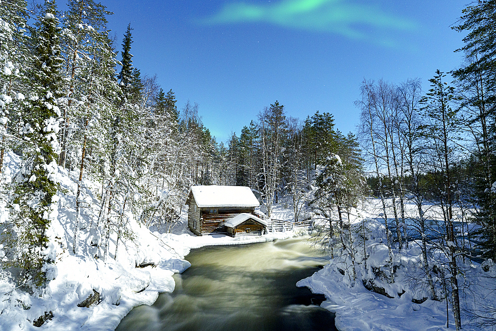 Aurora Borealis (Northern Lights) over a chalet overlooking Myllikoski rapids of frozen river, Ruka Kuusamo, Lapland, Finland, Europe