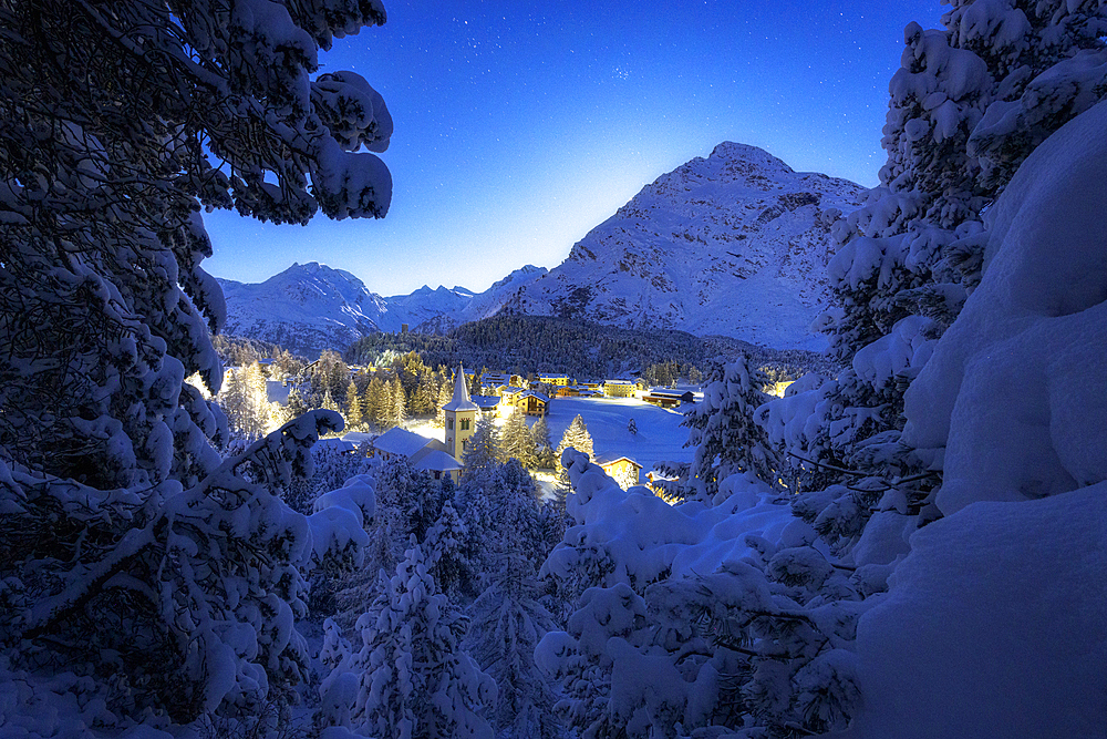 Fairy tale view of Chiesa Bianca covered with snow on a winter starry night, Maloja, Bregaglia, Graubunden, Engadin, Switzerland