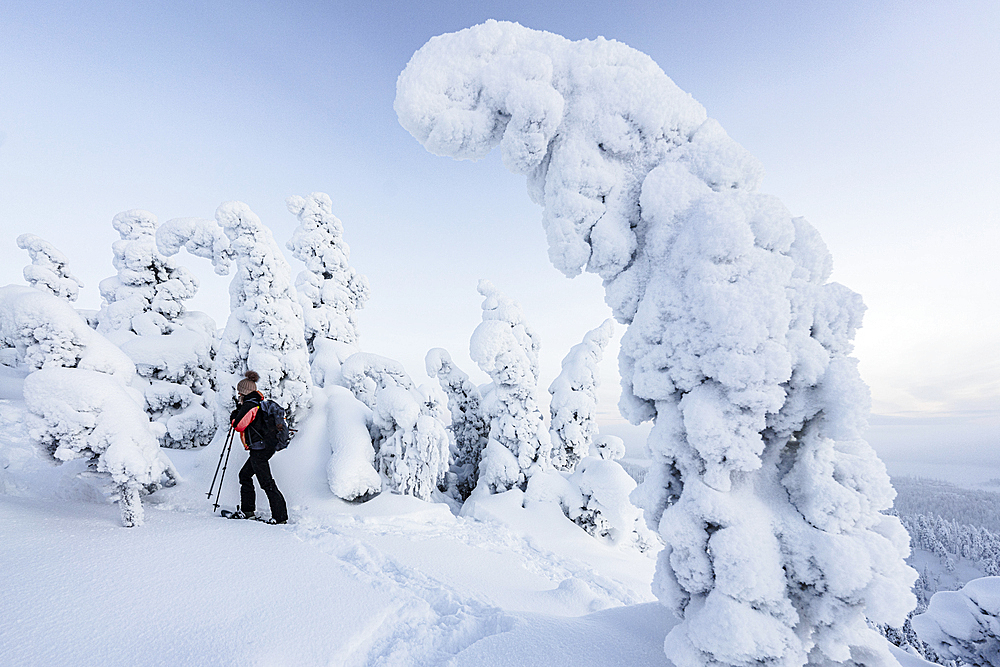 Mid adult woman with snowshoes looking at ice scupltures wrapped in snow, Oulanka National Park, Ruka Kuusamo, Lapland, Finland