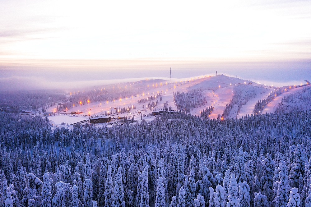 Mist at sunset over Ruka ski resort and snowy woods in winter, aerial view, Kuusamo, Northern Ostrobothnia, Lapland, Finland