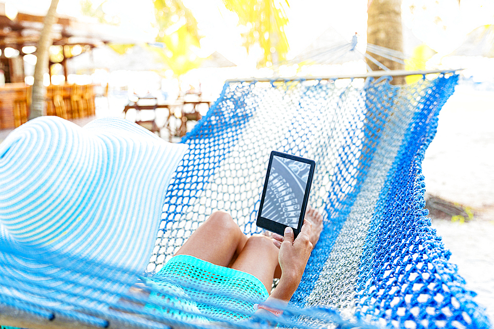 Woman reading from Kindle tablet lying on hammock, Zanzibar, Tanzania, East Africa, Africa