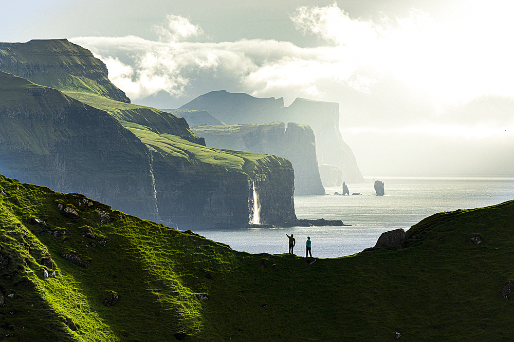 Silhouette of hikers admiring cliffs standing on top of mountain ridge above the ocean, Kalsoy island, Faroe Islands, Denmark, Europe