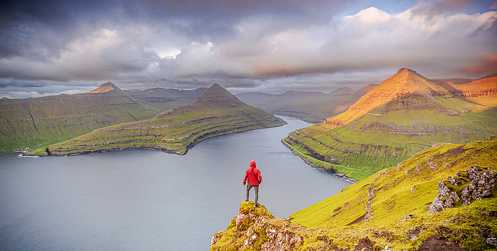 One man contemplating the sky at dawn standing on rocks above a fjord, Eysturoy Island, Faroe Islands, Denmark, Europe