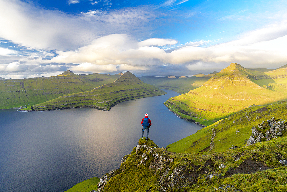 Hiker with backpack enjoying the view standing on rocks overlooking Funningur fjord, Eysturoy Island, Faroe Islands, Denmark, Europe