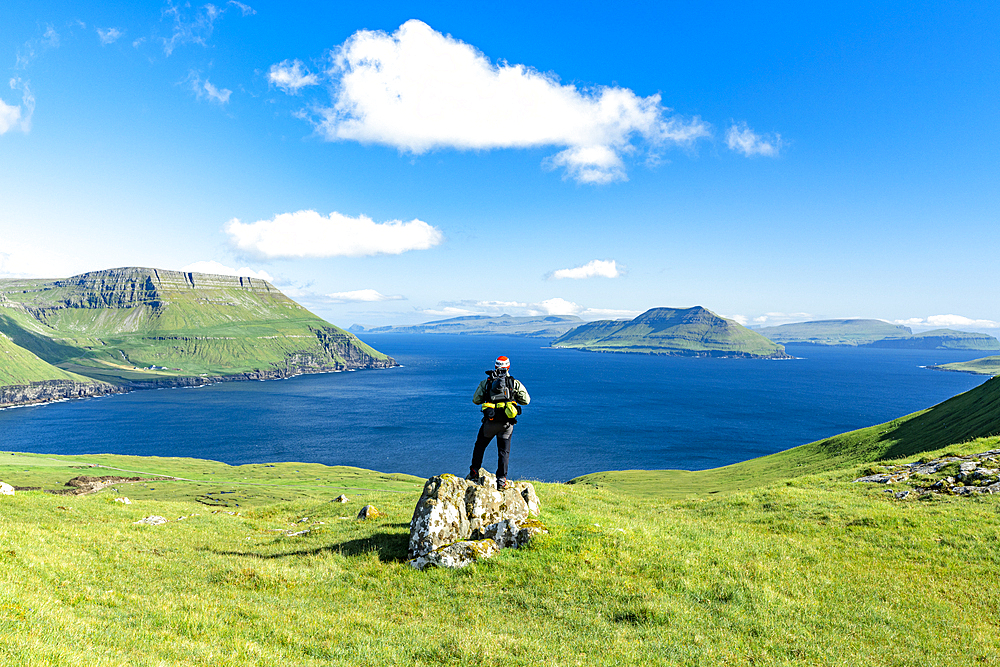 Hiker standing on top of rock contemplating the fjord in summer, Nordradalur, Streymoy Island, Faroe Islands, Denmark, Europe