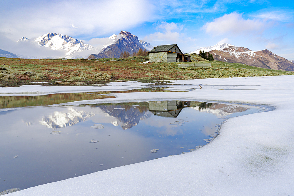 Mountain hut on shore of frozen pond during thaw, Scermendone Alp, Rhaetian Alps, Valtellina, Lombardy, Italy, Europe