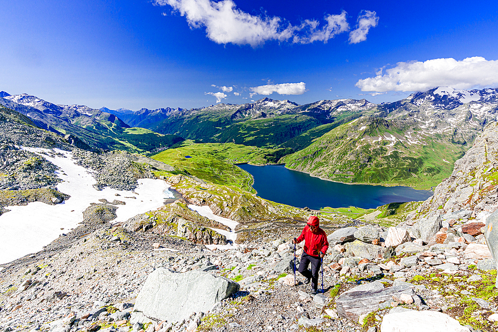 Hiker walking on mountain ridge above the blue lake Montespluga, Madesimo, Valle Spluga, Valtellina, Lombardy, Italy, Europe