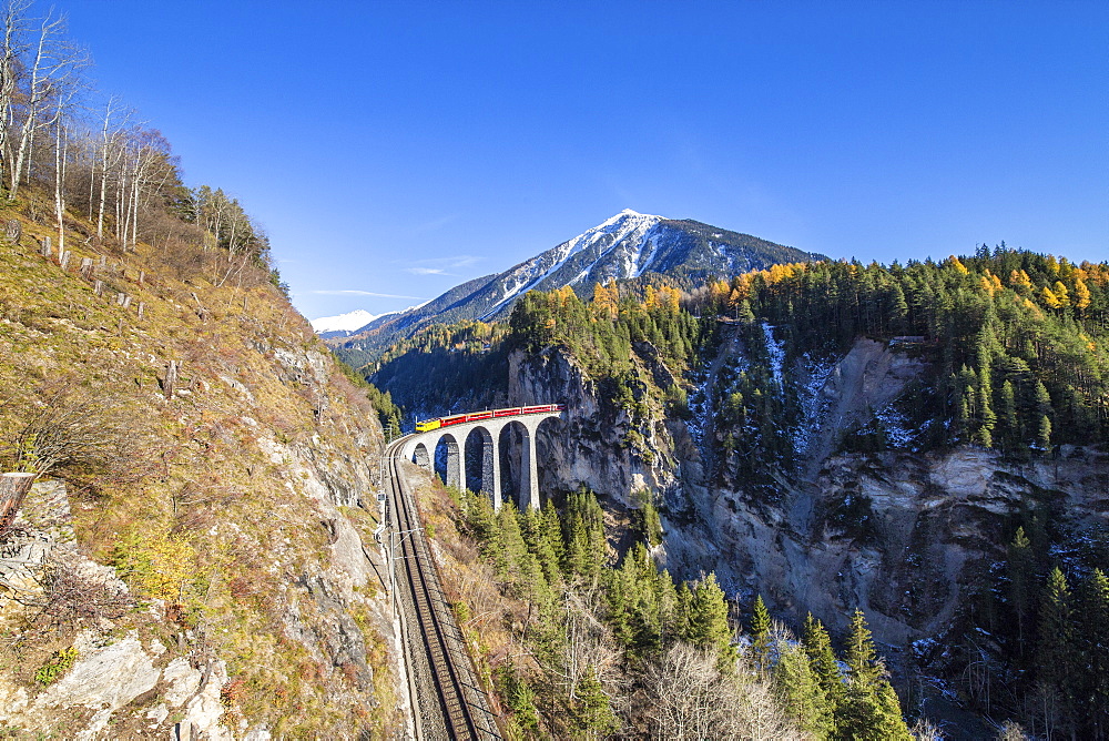 Bernina Express passes over the Landwasser Viadukt surrounded by colorful woods, Canton of Graubunden, Switzerland, Europe