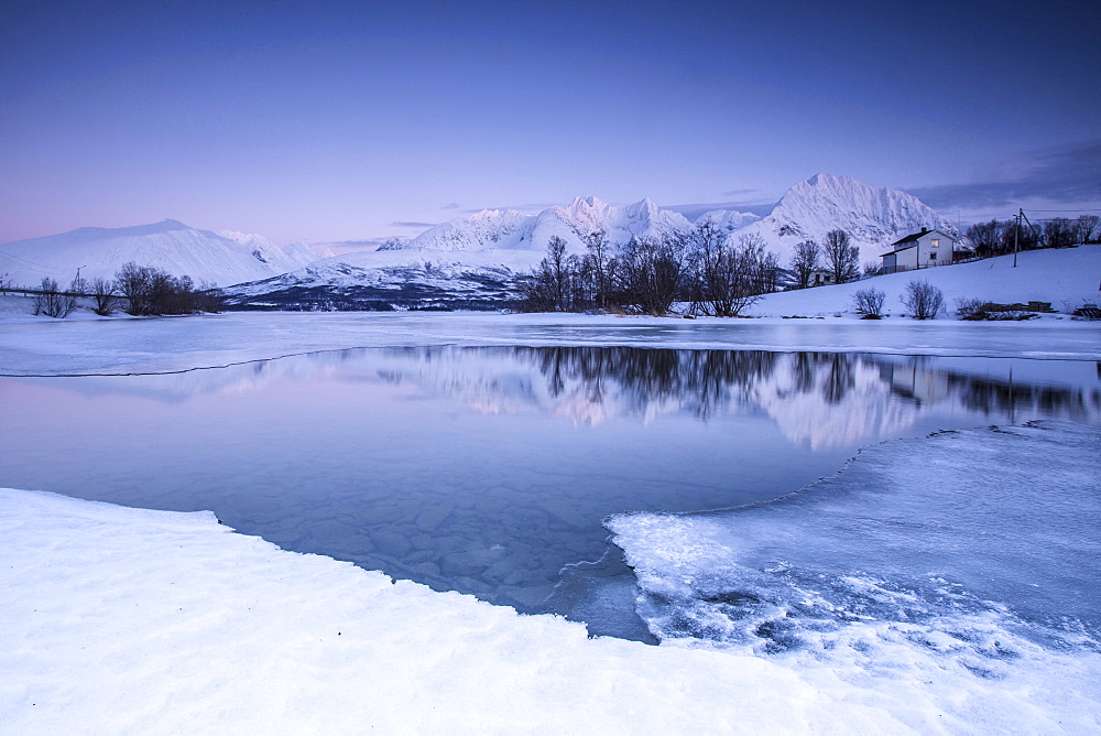 Snowy peaks are reflected in the frozen Lake Jaegervatnet at dusk, Stortind, Lyngen Alps, Troms, Lapland, Norway, Scandinavia, Europe