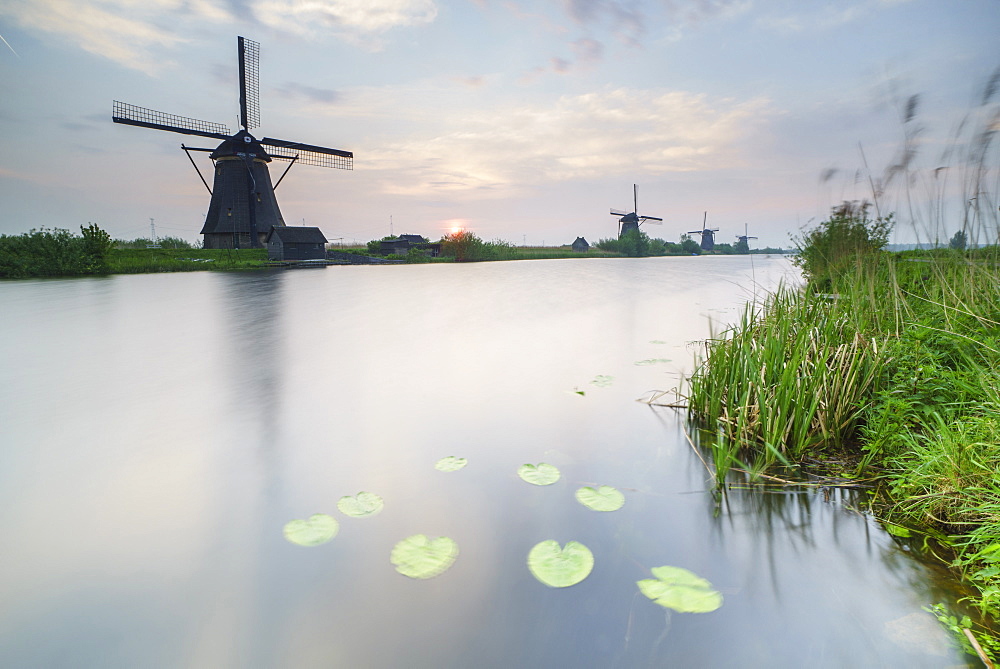 Blue sky and pink clouds on the windmills reflected in the canal at dawn, Kinderdijk, Rotterdam, South Holland, Netherlands, Europe