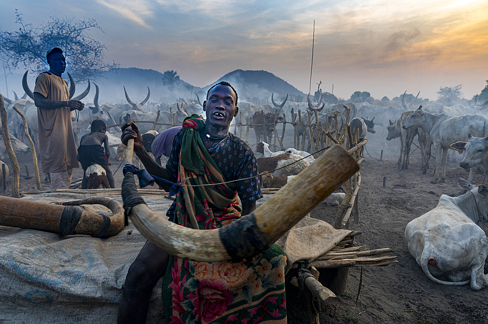 Man blowing a massive cow horn to signal the cows to come back, Mundari tribe, South Sudan, Africa