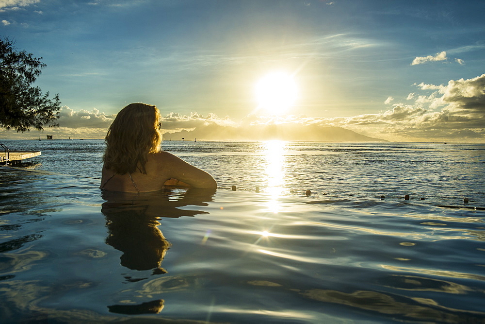 Woman enjoying the sunset in a swimming pool with Moorea in the background, Papeete, Tahiti, Society Islands, French Polynesia, Pacific