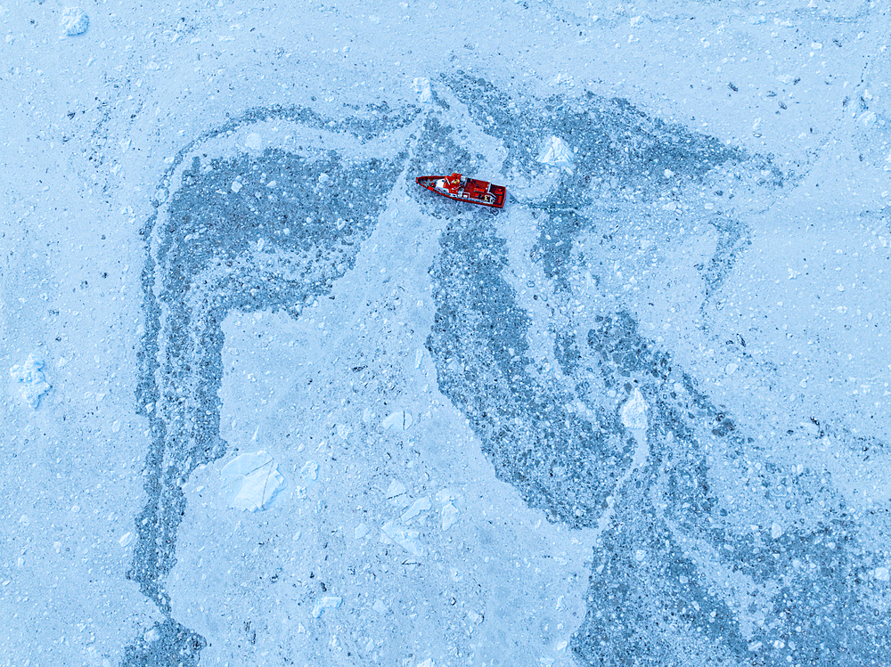 Aerial of a little ship floating between the ice below the Eqi glacier, Western Greenland