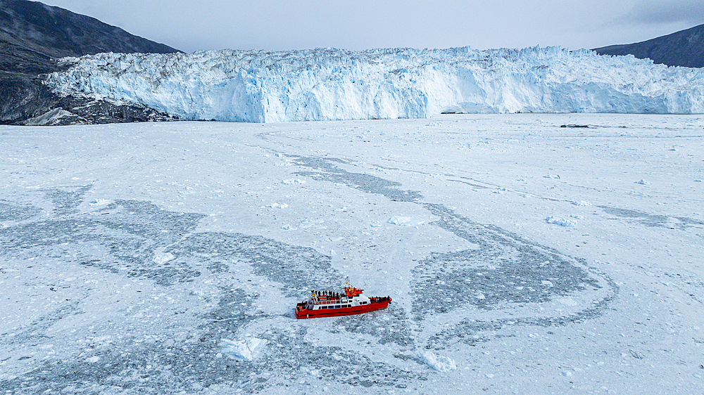 Aerial of a little ship floating between the ice below the Eqi glacier, Western Greenland, Denmark, Polar Regions