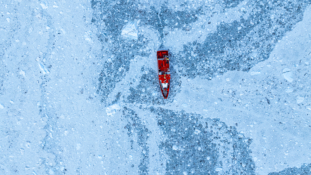 Aerial of a little ship floating between the ice below the Eqi glacier, Western Greenland