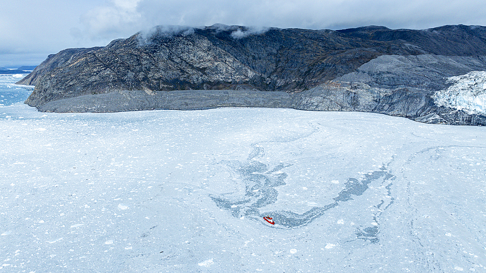 Aerial of a little ship floating between the ice below the Eqi glacier, Western Greenland, Denmark, Polar Regions