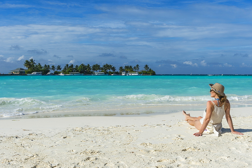 Woman sitting on a white sand beach enjoying the turquoise water, Sun Island Resort, Nalaguraidhoo island, Ari atoll, Maldives, Indian Ocean, Asia