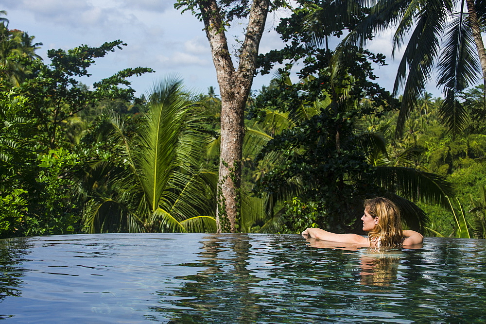 Woman enjoying an overflowing pool above a valley in the Kamandalu Ubud resort, Ubud, Bali, Indonesia, Southeast Asia, Asia