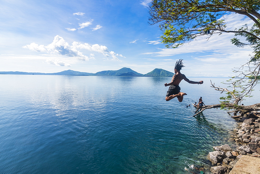 Man jumping in the bay of Rabaul with Volcano Tavurvur in the background, East New Britain, Papua New Guinea, Pacific