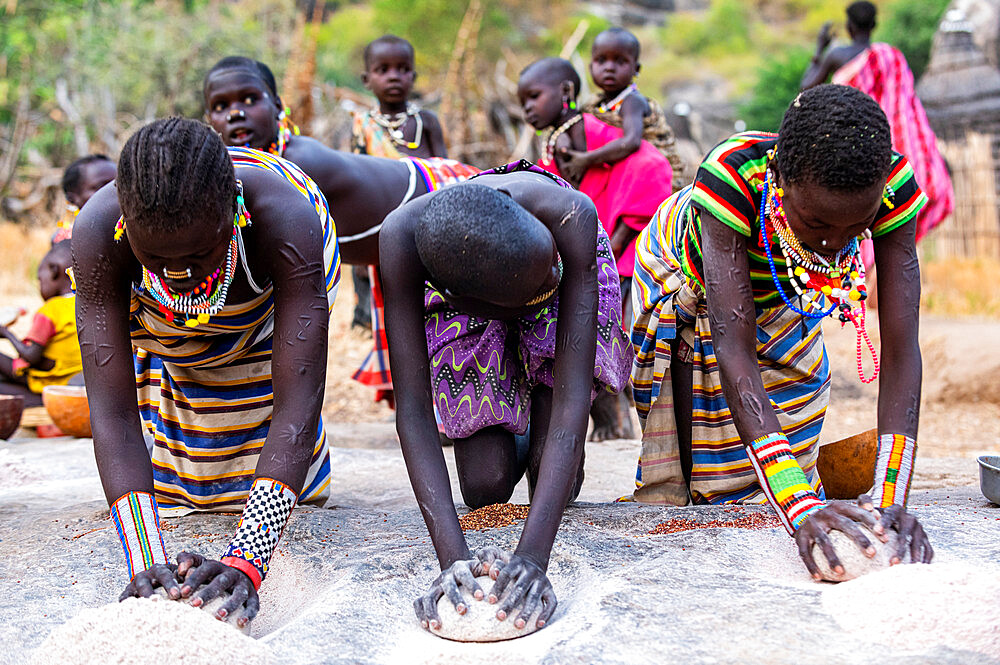 Young girls grinding Sorghum on a rock, Laarim tribe, Boya Hills, Eastern Equatoria, South Sudan, Africa