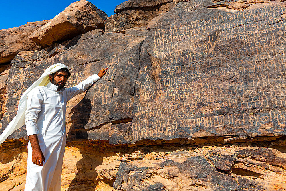 Man pointing at rock carvings, Bir Hima Rock Petroglyphs and Inscriptions, UNESCO World Heritage Site, Najran, Kingdom of Saudi Arabia, Middle East