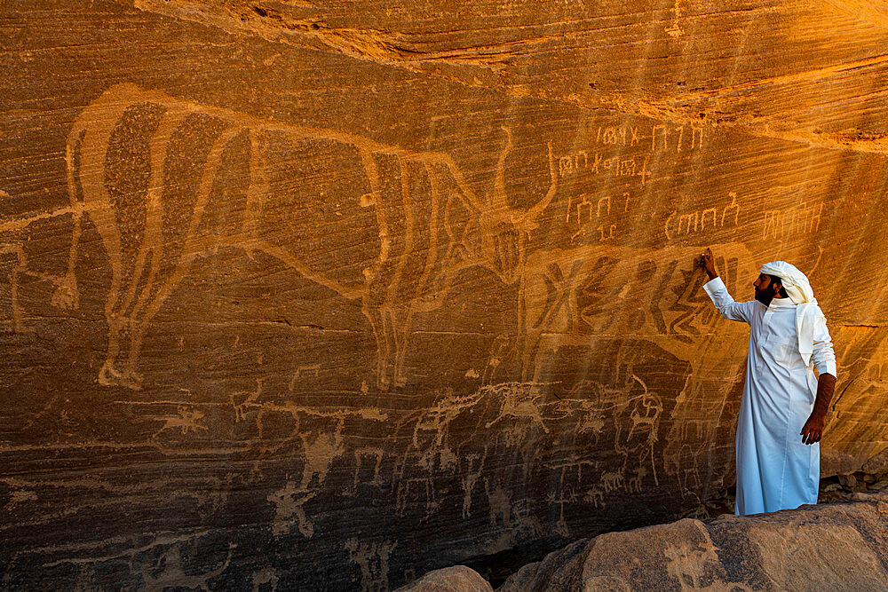 Man pointing at rock carvings, Bir Hima Rock Petroglyphs and Inscriptions, UNESCO World Heritage Site, Najran, Kingdom of Saudi Arabia, Middle East