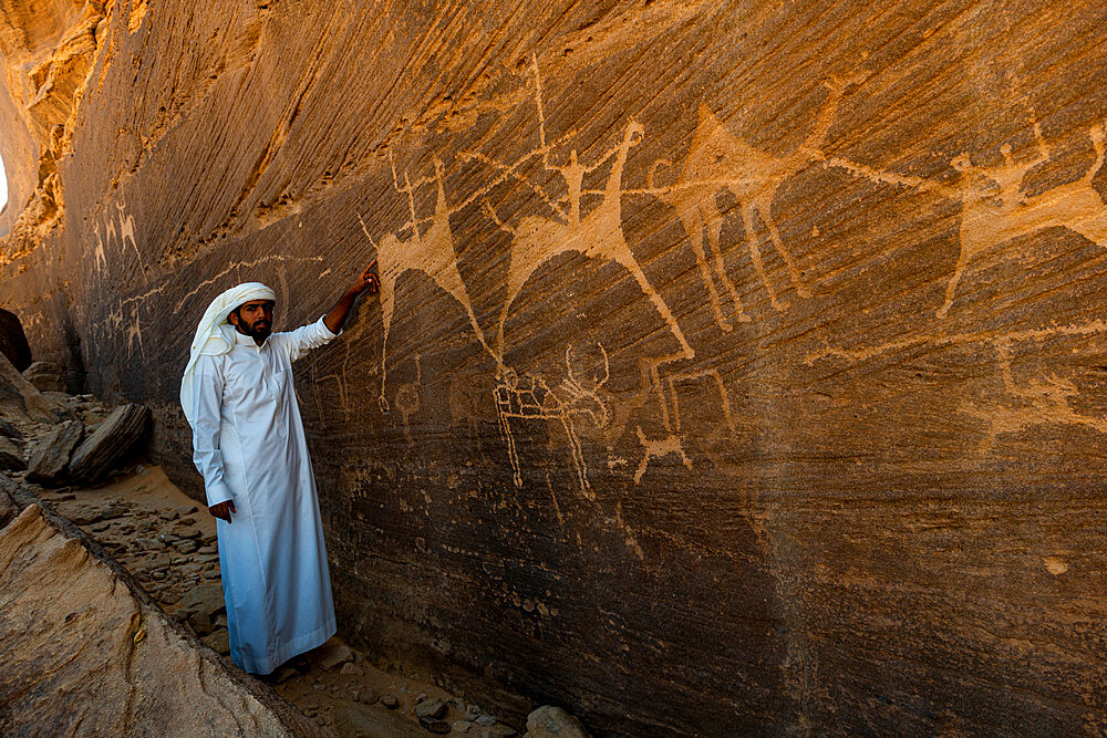 Man pointing at rock carvings, Bir Hima Rock Petroglyphs and Inscriptions, UNESCO World Heritage Site, Najran, Kingdom of Saudi Arabia, Middle East