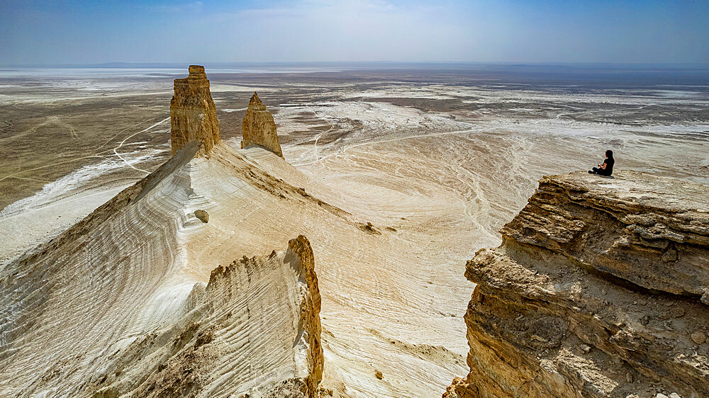 Woman sitting on a giant rock cliff, Bozzhira Canyon, Ustyurt plateau, Mangystau, Kazakhstan, Central Asia, Asia