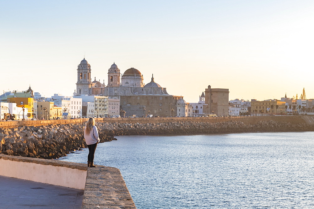 Woman enjoying the view of Santa Cruz Cathedral and ocean seen from the promenade along quayside, Cadiz, Andalusia, Spain, Europe