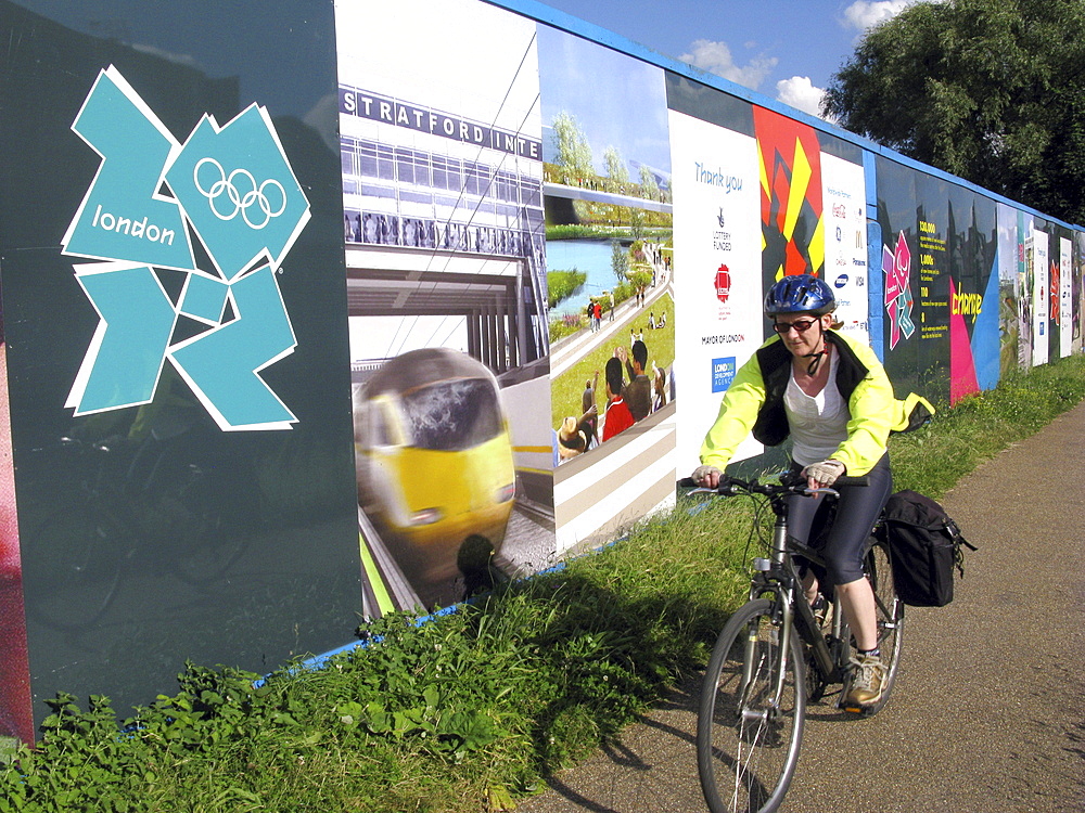 Uk cyclist going past the fence around the olympic park sorrounding construction of the facilities and the site of the future olympic stadium in east london