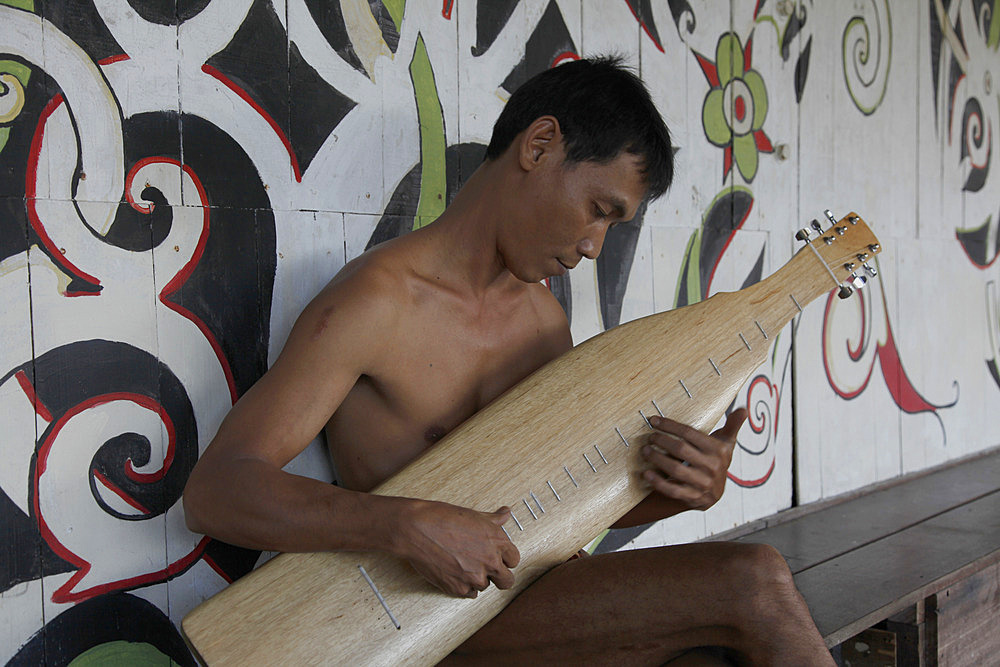 Iban man playing traditional instrument in a native Iban longhouse in Borneo, Malaysia, Southeast Asia, Asia