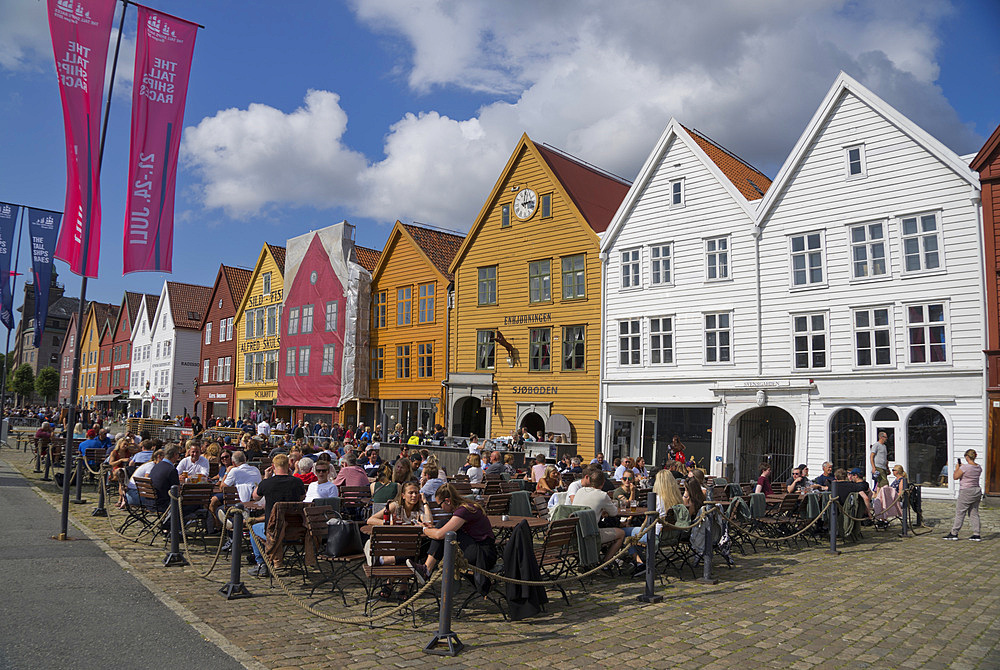 Tourists sit in the sun in outdoor bars and cafes in the old wharf and traditional wooden buildings in the Bryggen quarter of Bergen, UNESCO World Heritage Site, Norway, Scandinavia, Europe