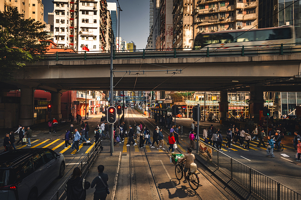 A street scene of Hong Kong with a Hong Kong Tram in the Background with pedestrians crossing a busy street in Hong Kong