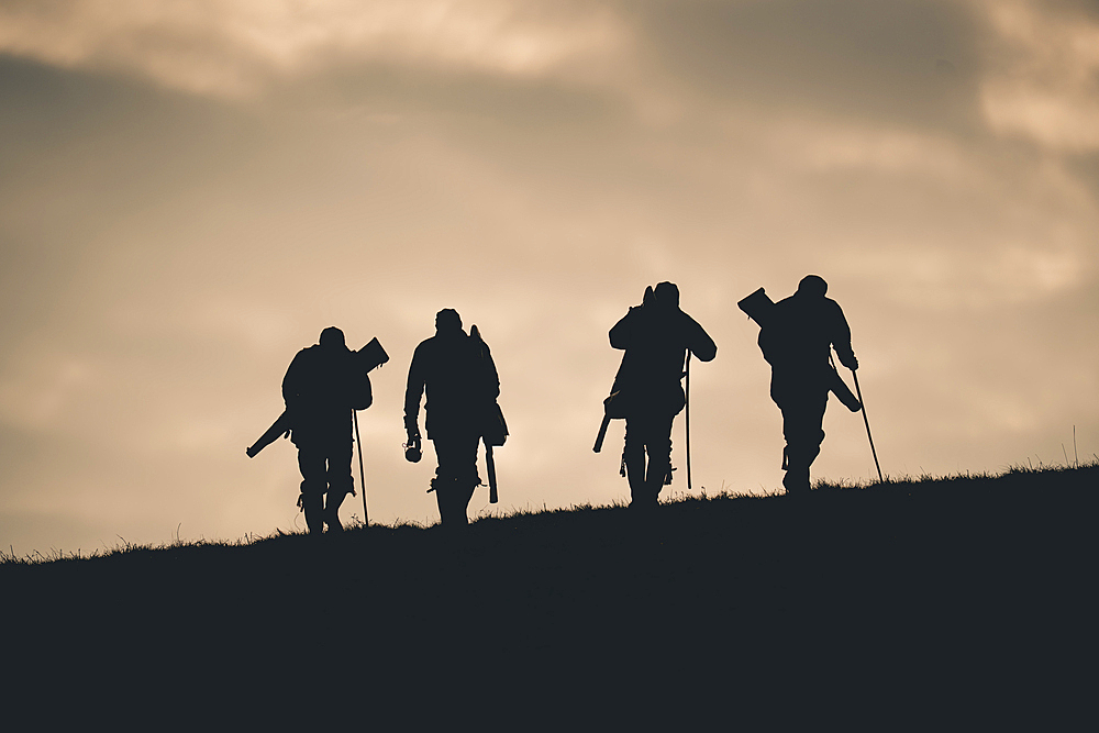 A silhouette of guns with their guns and walking sticks towards the next drive on a pheasant shoot in UK