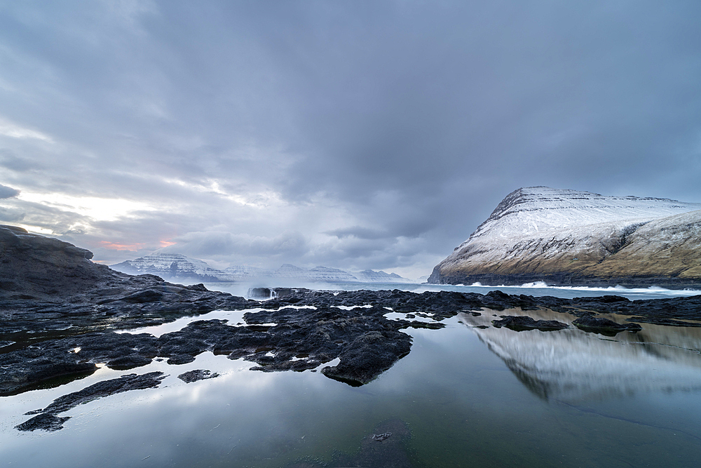 Snow covered mountains and rock pool reflections at low tide, Gjogv village, Eysturoy Island, Faroe Islands, Denmark, Europe